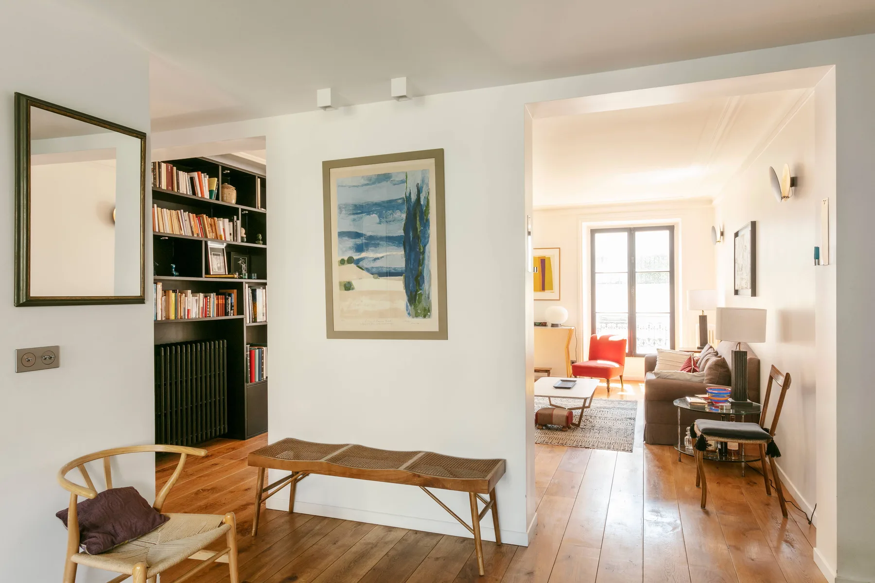 Una sala luminosa con suelo de madera, estanterías y asientos.