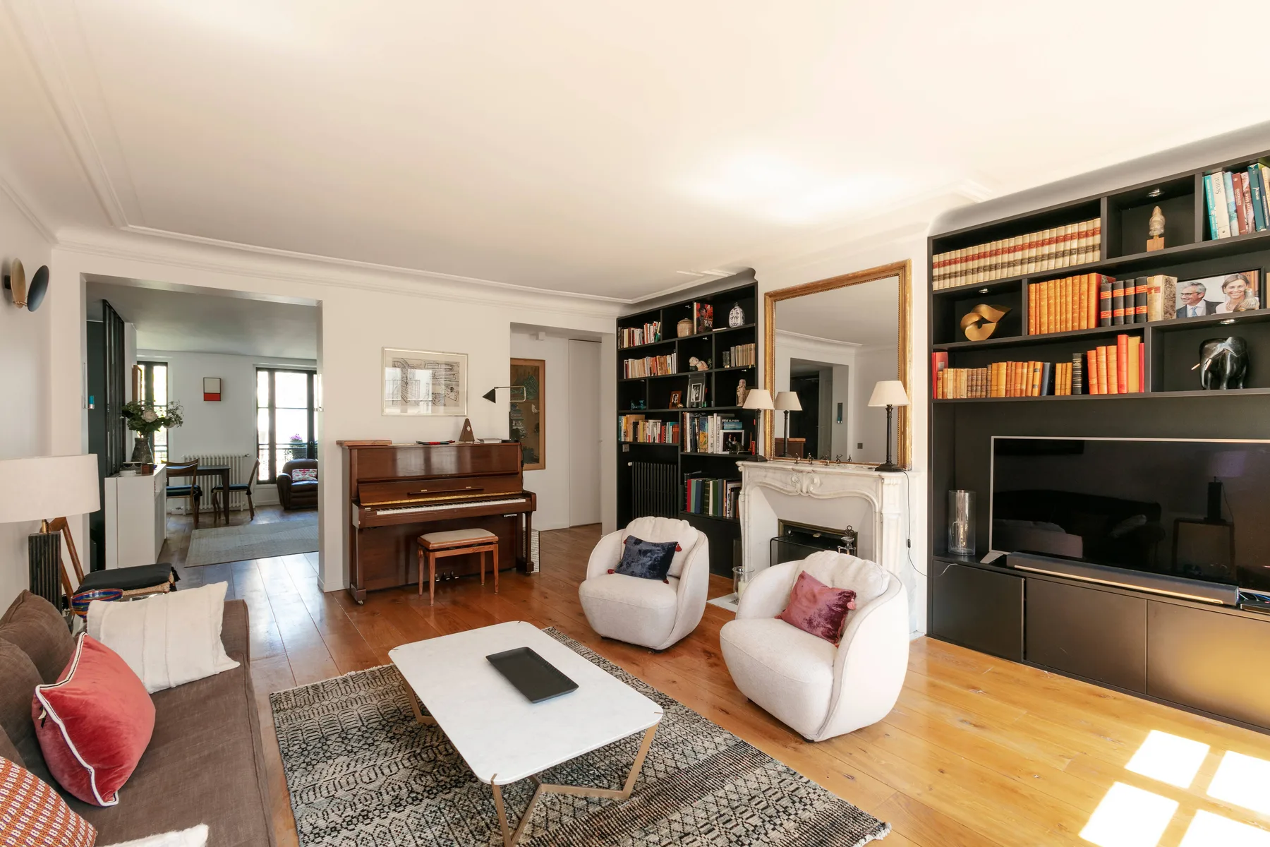 Sala de estar con asientos, un televisor, estanterías y un piano.