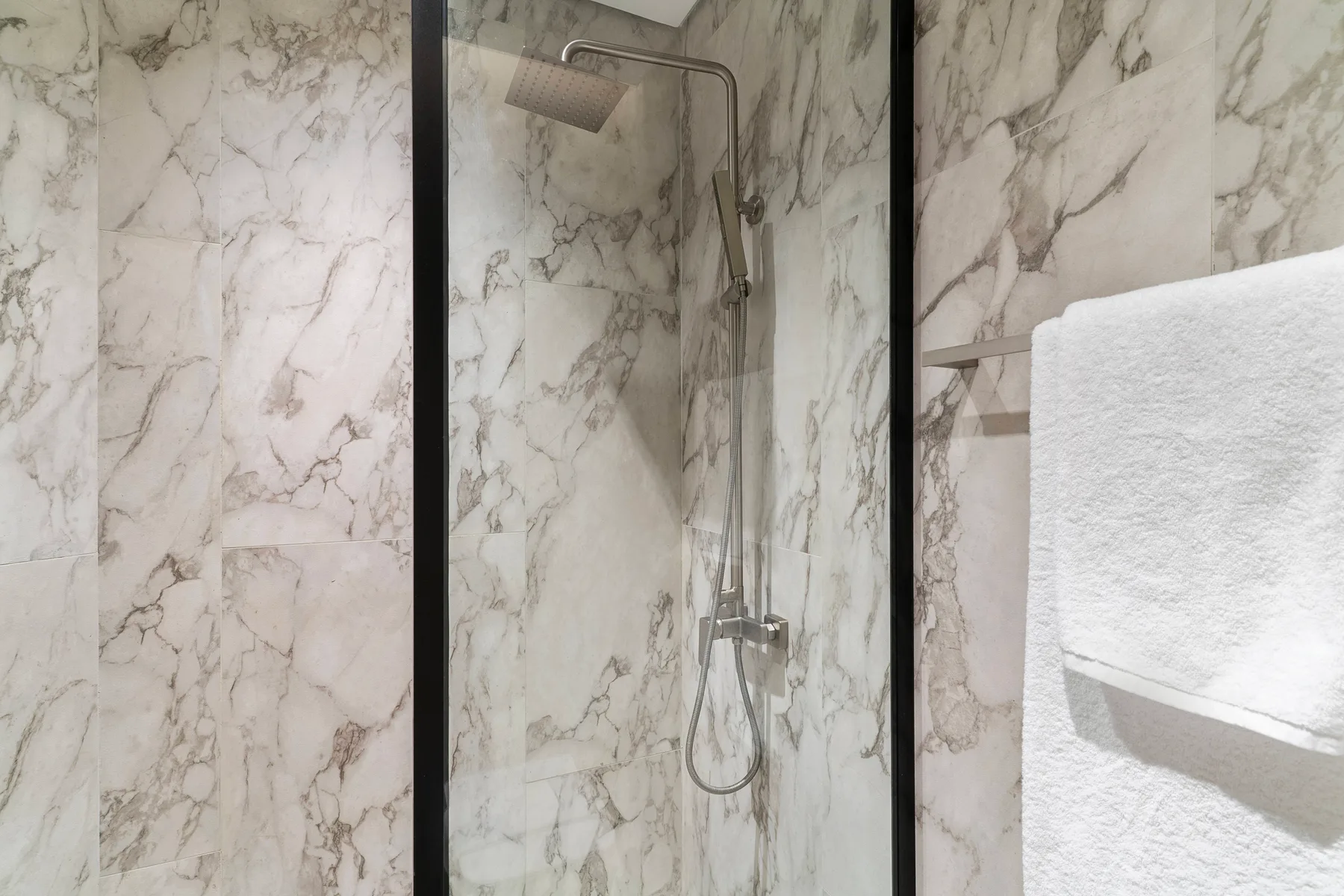 Una ducha de baño con azulejos, una alcachofa de mano y una toalla blanca.