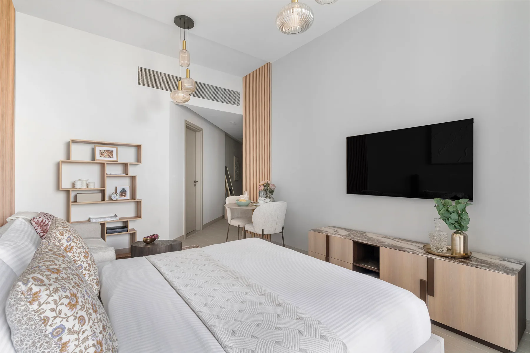 Un dormitorio luminoso con una cama bien tendida y un televisor en la pared.