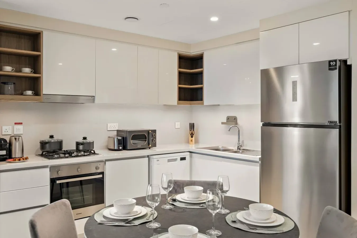Una cocina moderna con gabinetes blancos, electrodomésticos de acero inoxidable y una mesa de comedor.