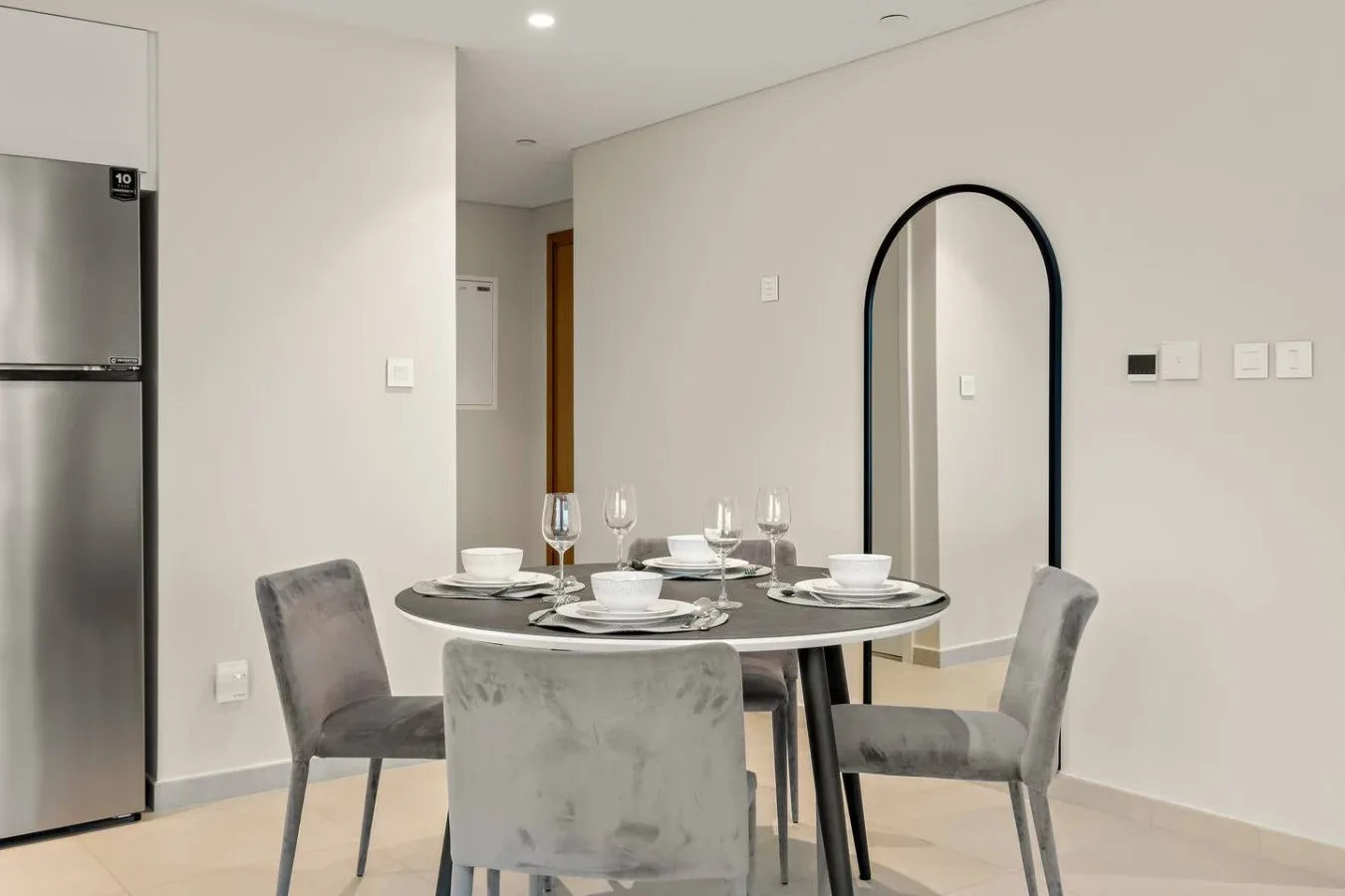 Comedor con mesa puesta, asientos grises y un espejo alto de arco.