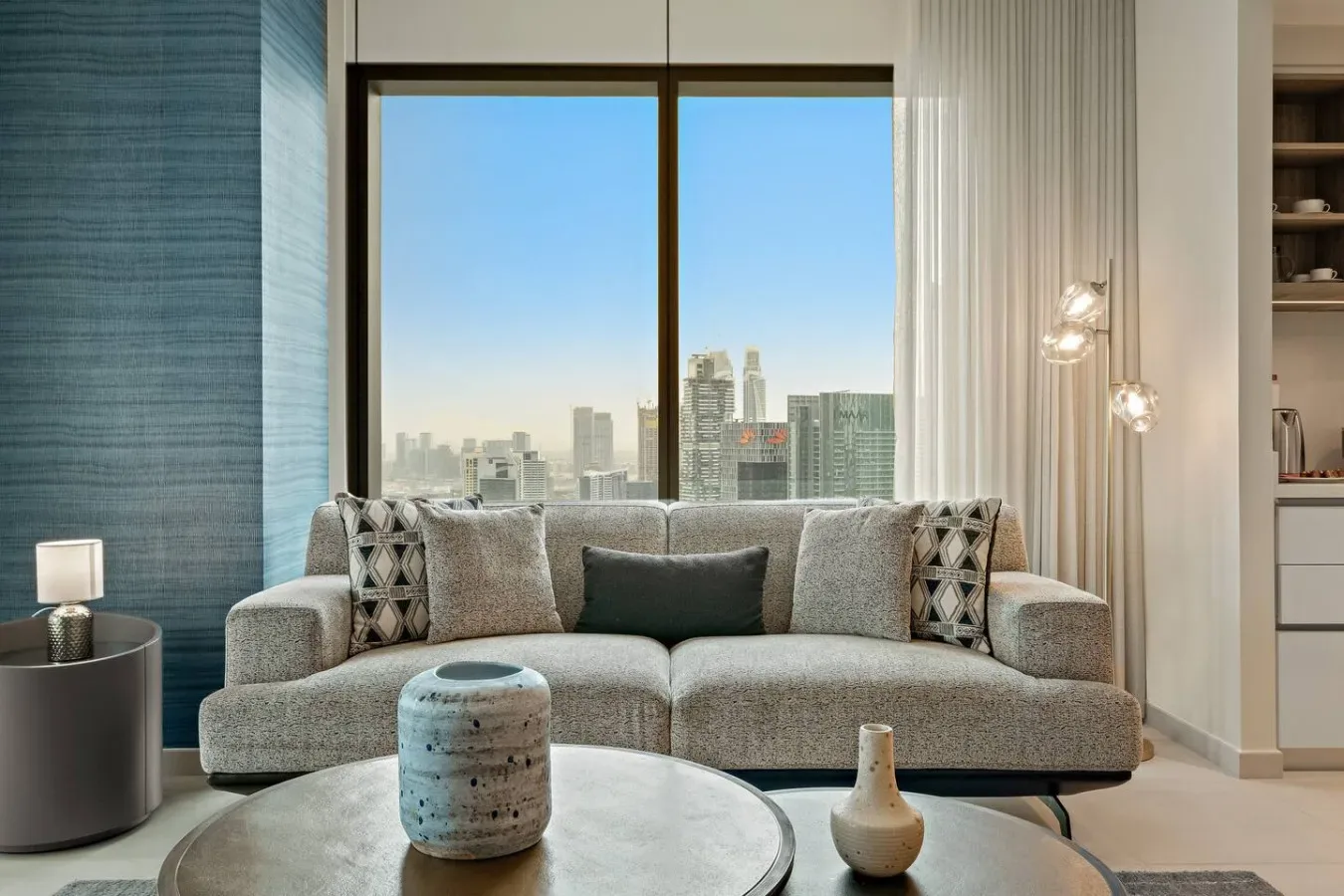 Una sala de estar con un sofá grande frente a ventanales con vistas al horizonte urbano.
