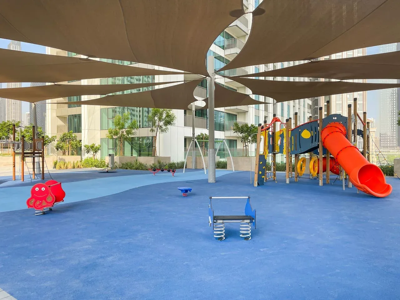 Un parque infantil con sombra y juegos coloridos sobre una superficie azul.