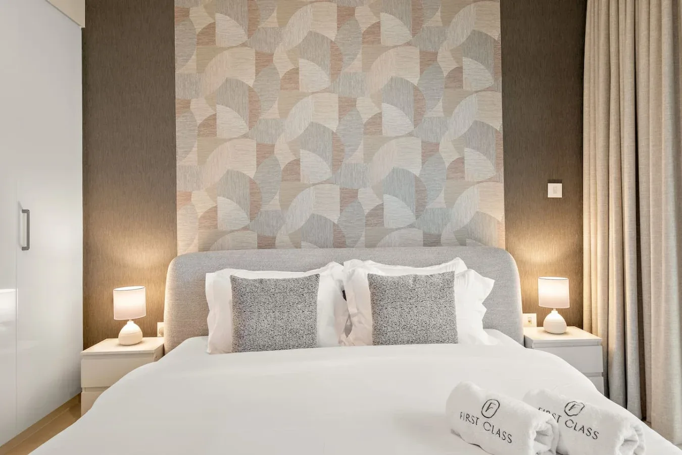 Un dormitorio con una cama bajo un panel de pared estampado y lámparas de noche.