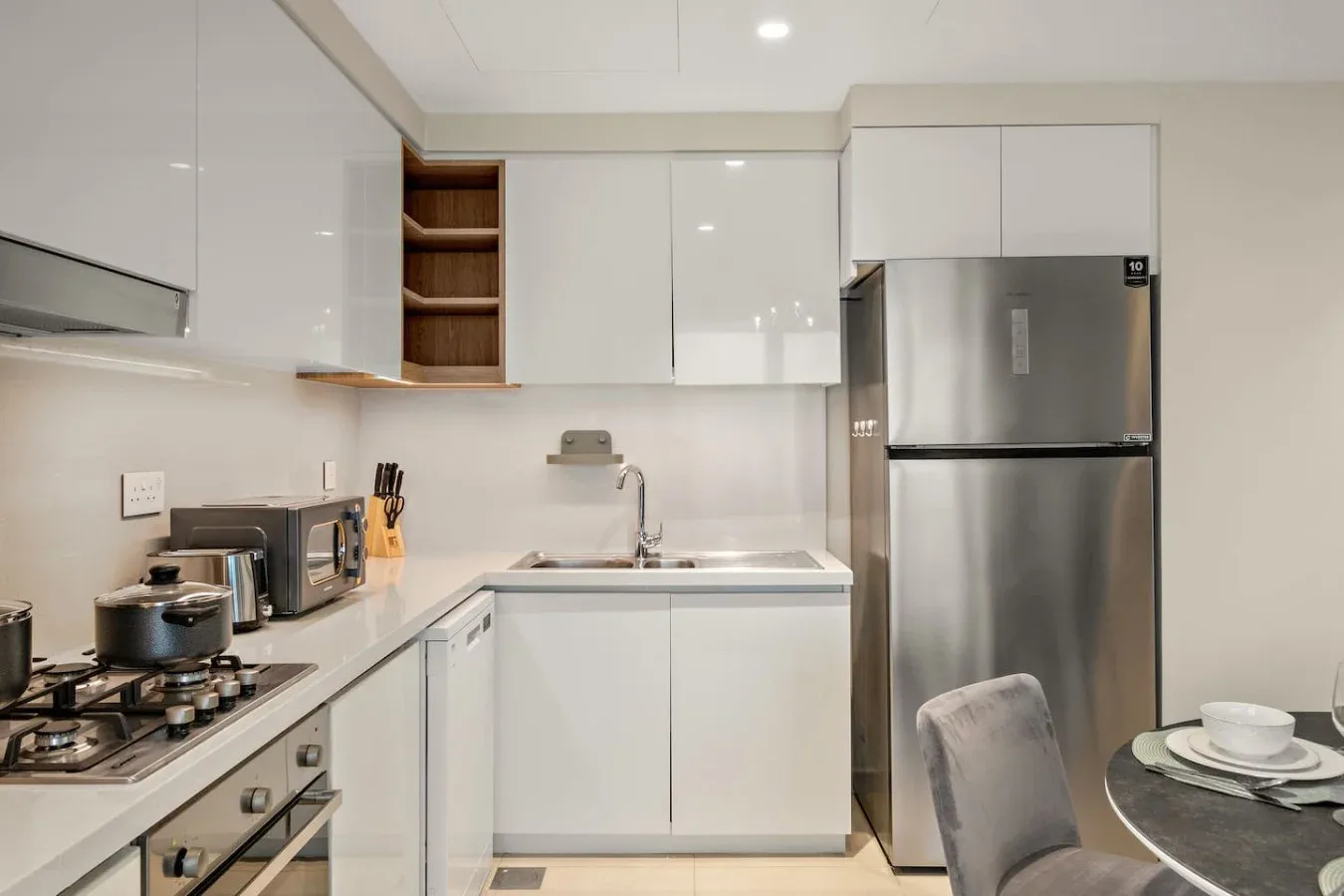Una cocina moderna con gabinetes blancos, un refrigerador de acero inoxidable y una mesa de comedor.