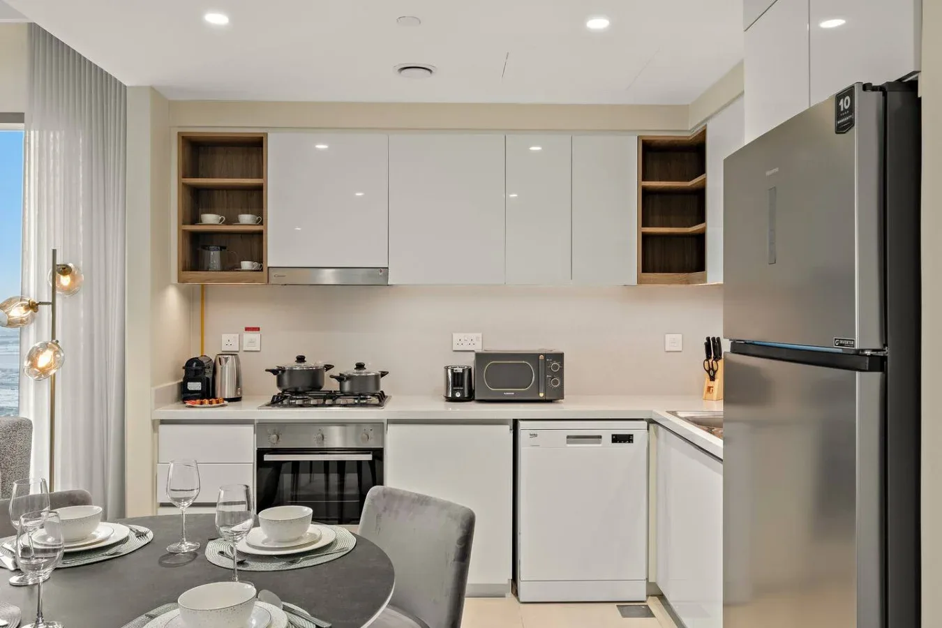 Una cocina moderna con gabinetes blancos, electrodomésticos de acero inoxidable y una mesa de comedor.