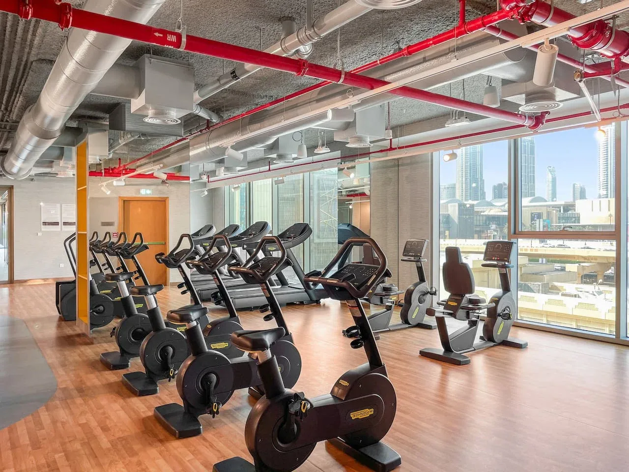 Una sala de ejercicios con bicicletas estáticas y cintas de correr junto a grandes ventanas.