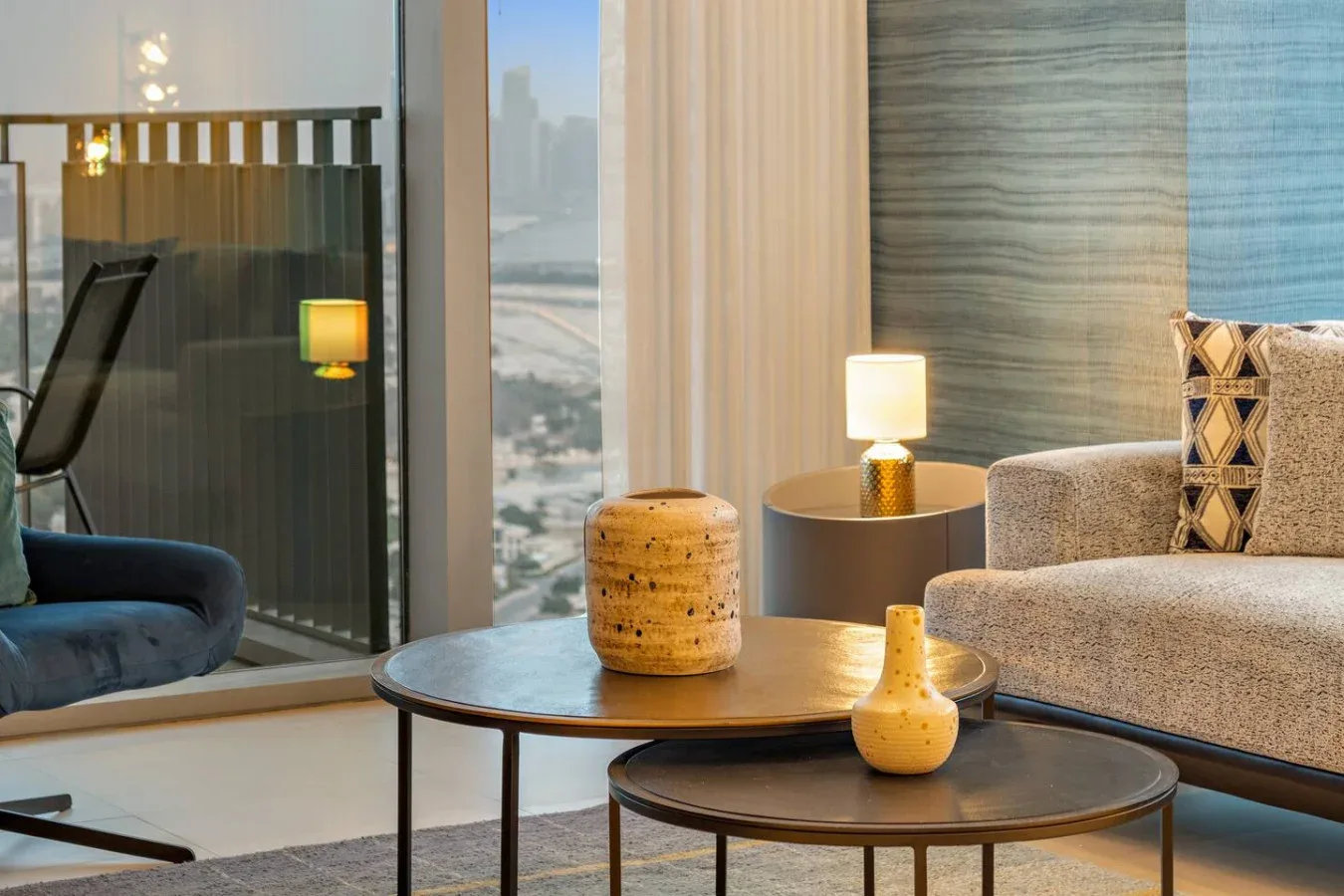 Una sala de estar moderna con asientos, mesas de centro y una vista de la ciudad por ventanales.