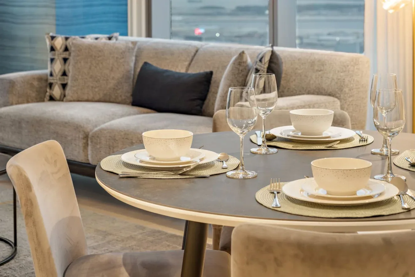 Un comedor con la mesa puesta frente a un sofá y grandes ventanales.