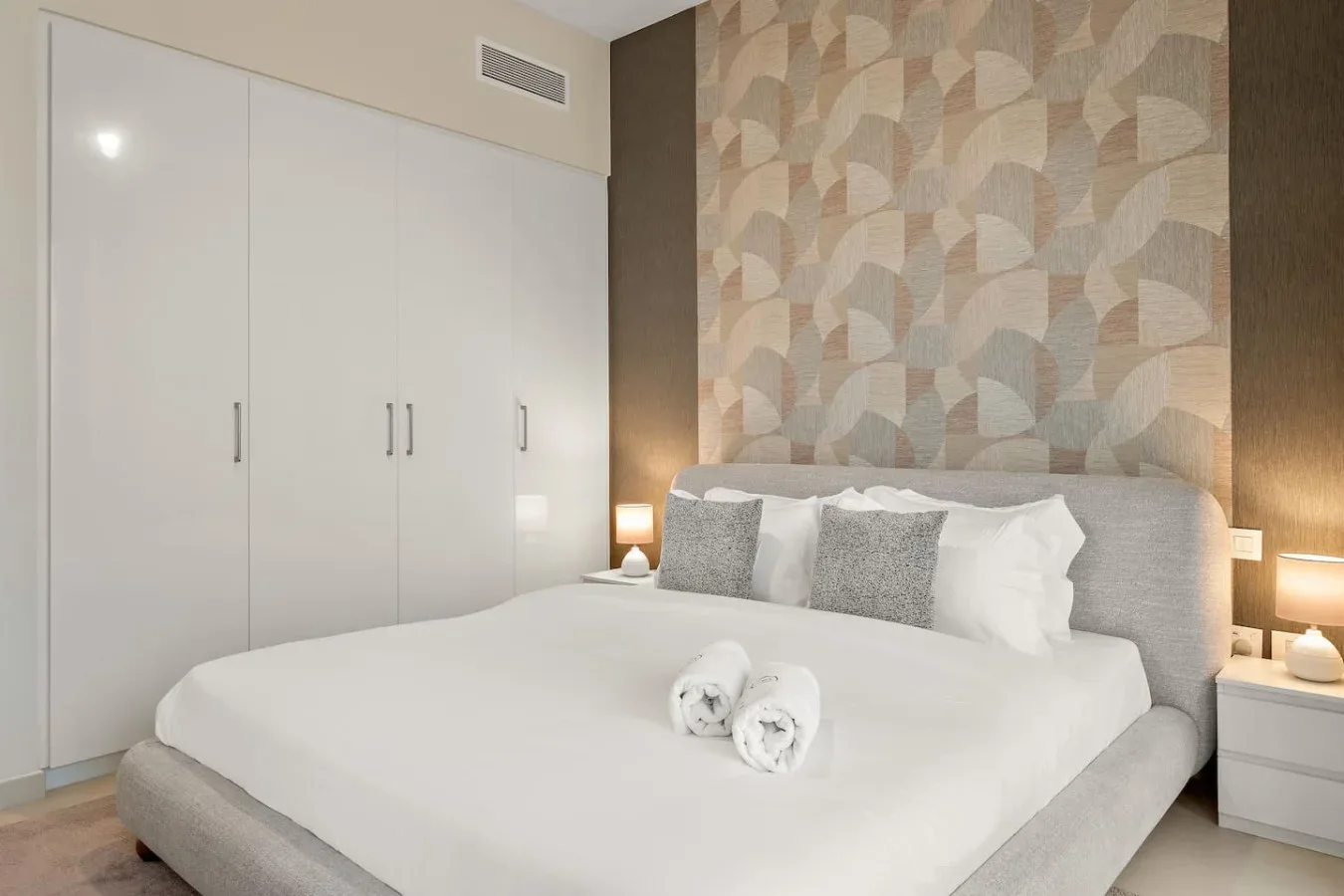 Un dormitorio con una cama bien tendida frente a una pared decorativa estampada.