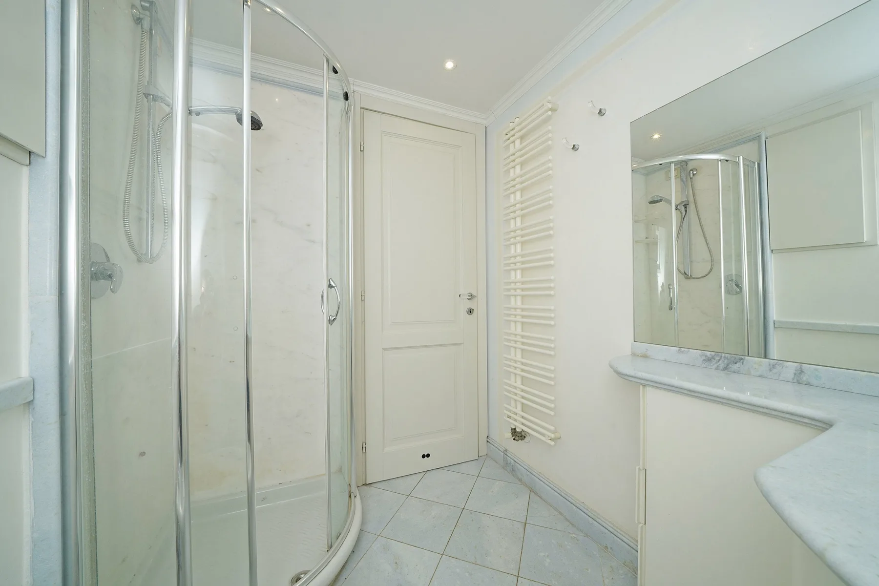 A bright bathroom with a glass shower, a wall mirror, and tiled flooring.