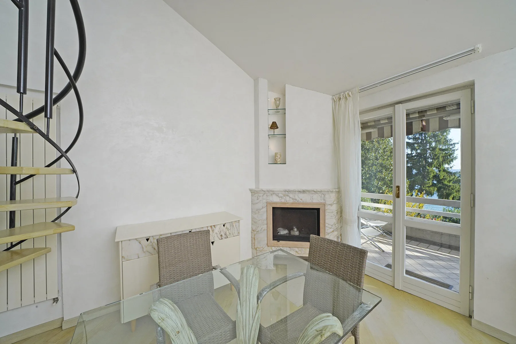 A bright dining area with a glass table beside a fireplace and balcony doors.