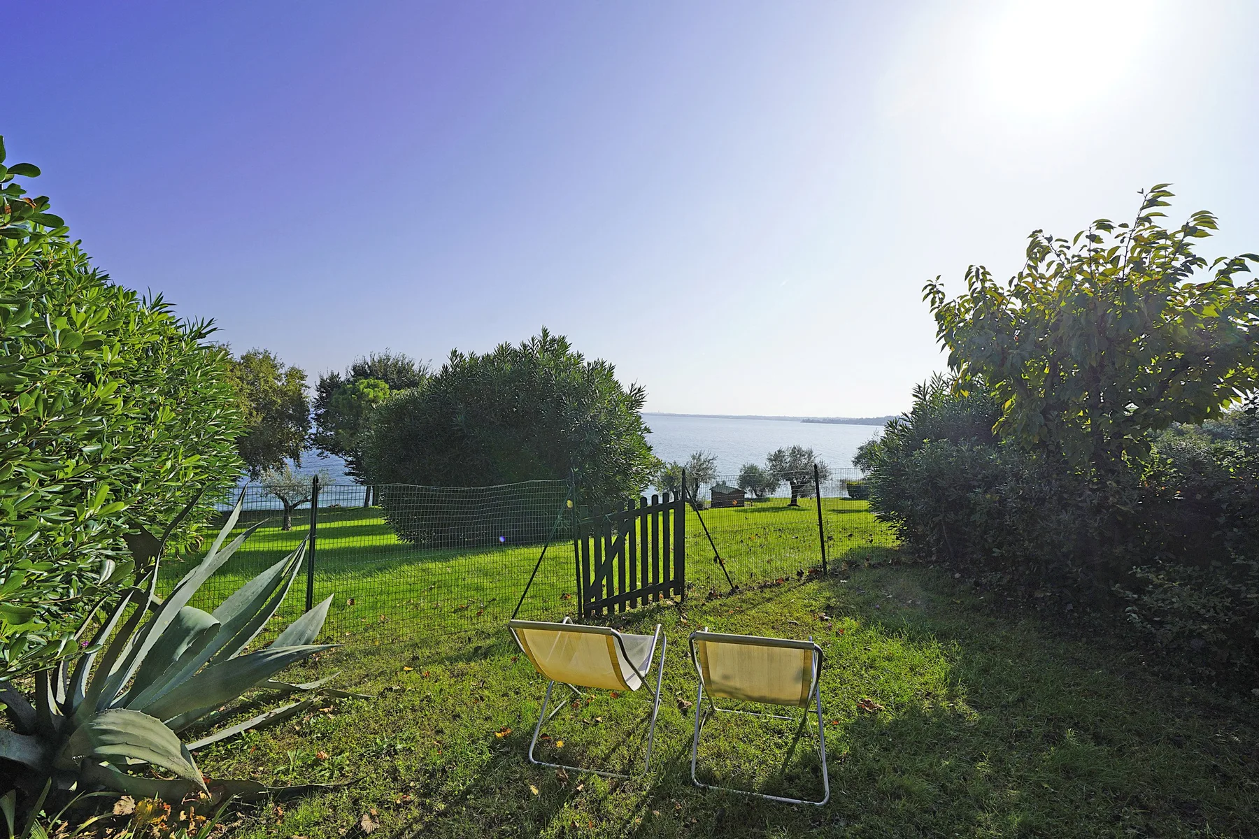 A grassy garden with two folding chairs overlooks the water.