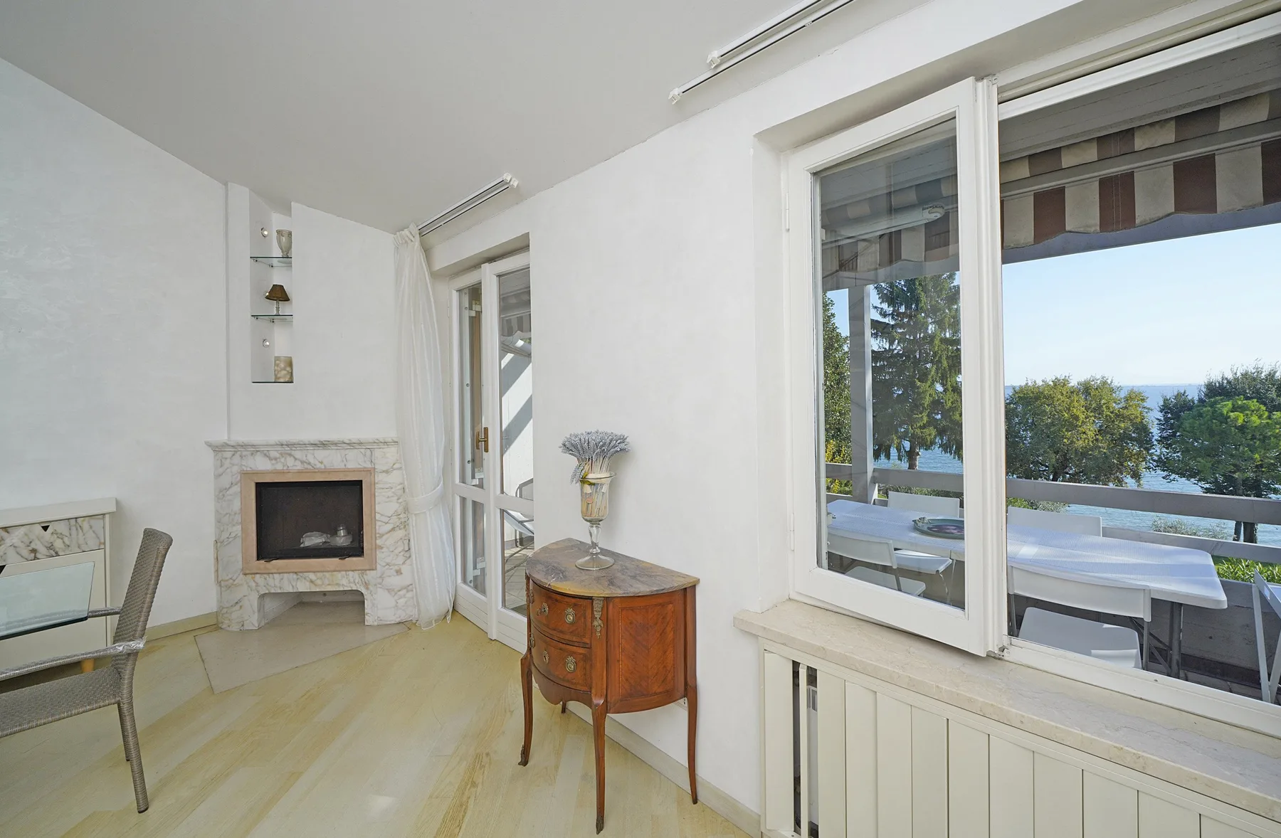 A bright sitting room with a fireplace and windows overlooking trees.