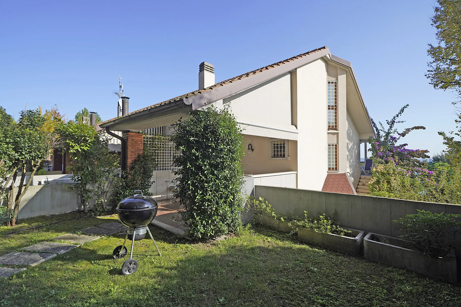 A house stands behind a garden with a barbecue grill in the foreground.