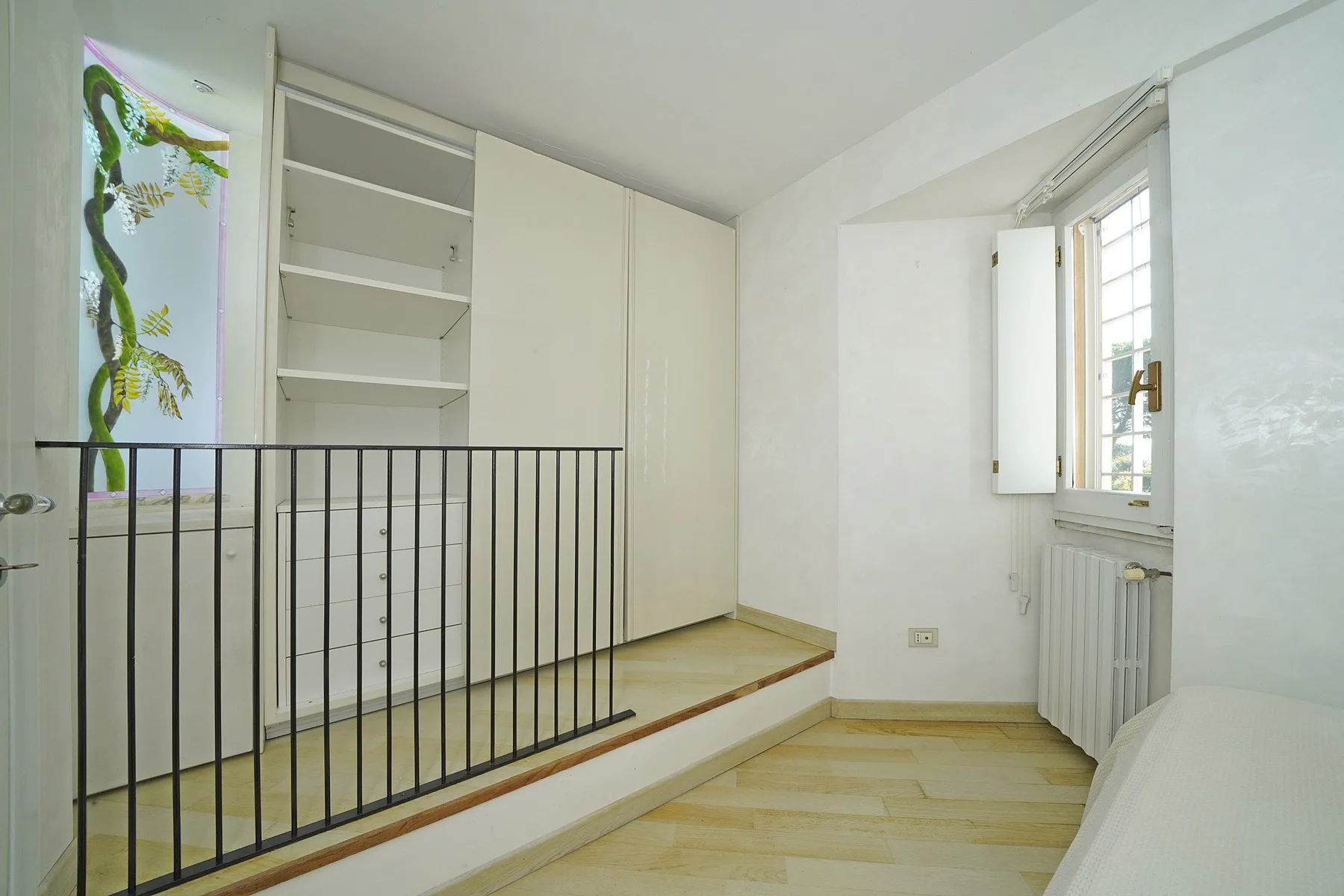 A bright room with built-in shelving, a window, and a low black railing.