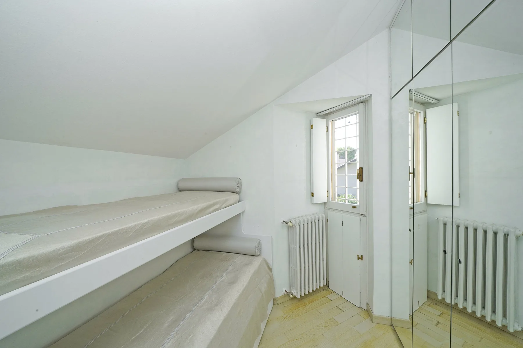 A bright attic bedroom with bunk beds, a window, and mirrored closet doors.