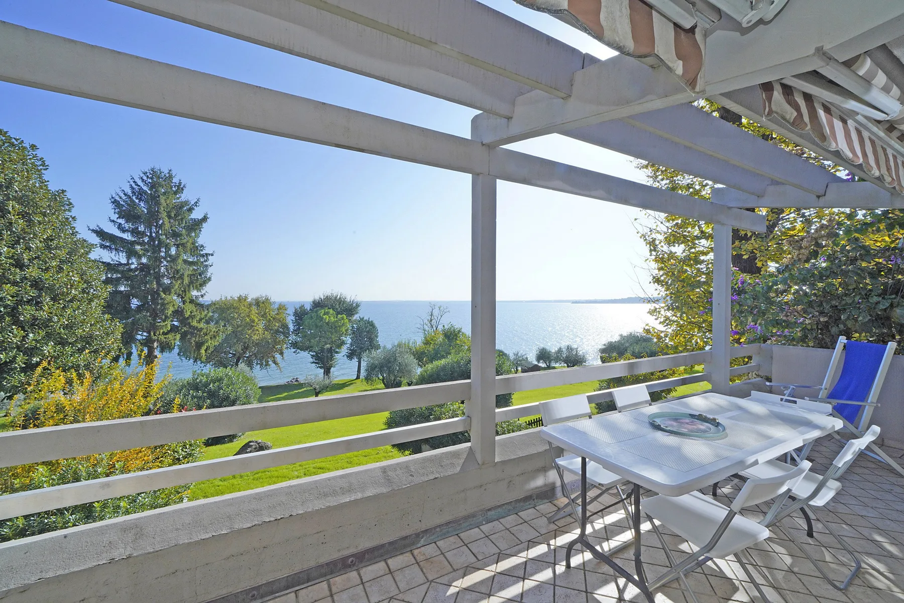 A furnished patio overlooks a lake beneath a white pergola.