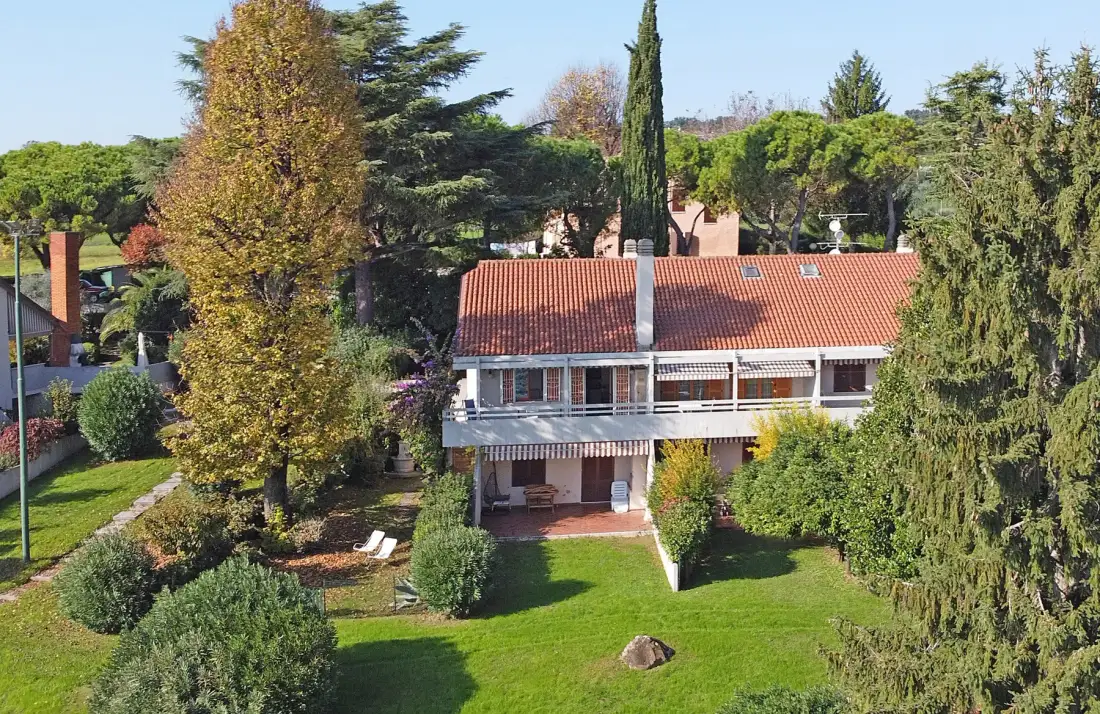 A house with a red tiled roof sits among trees and a broad green lawn.