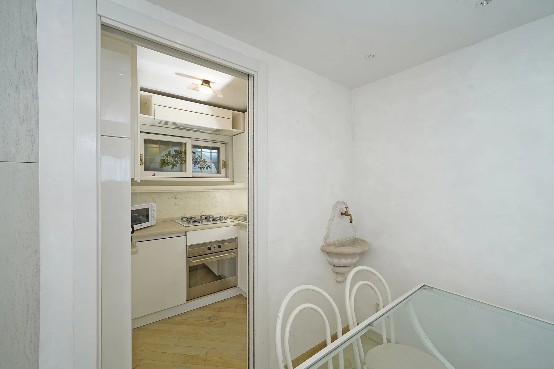 A bright dining area with a glass table beside an open kitchen.