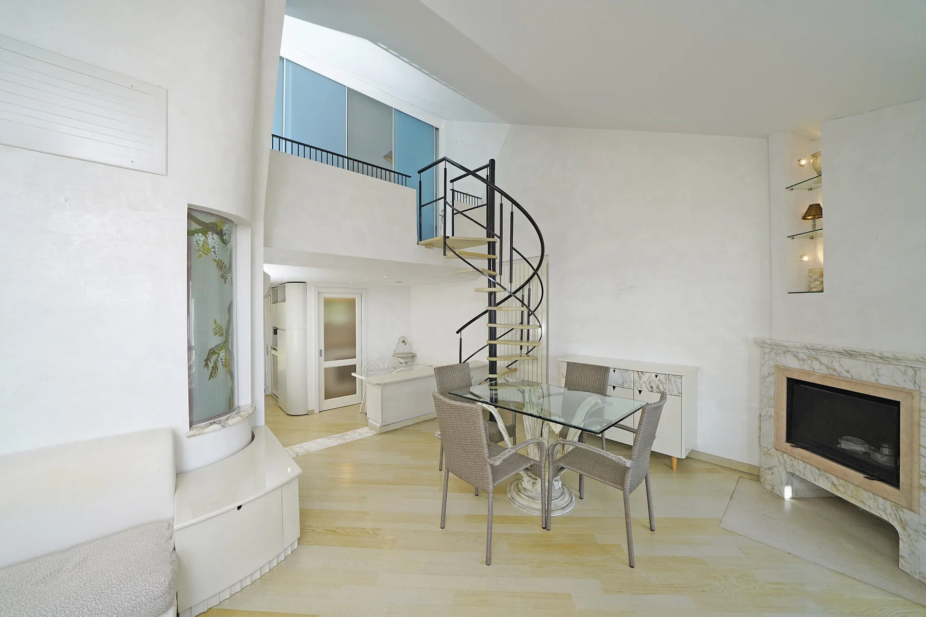 A bright living area with a spiral staircase and glass dining table.