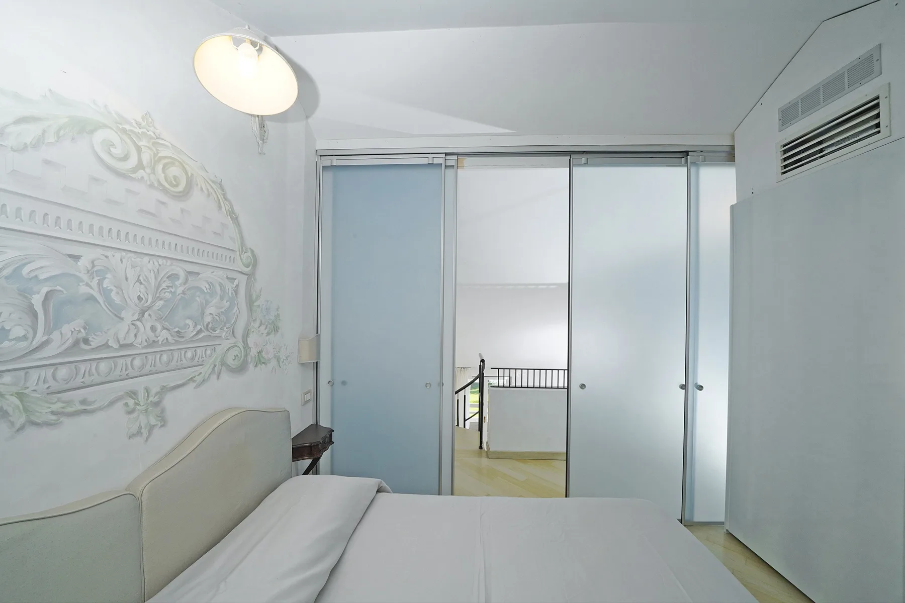 A bedroom with a bed facing sliding wardrobe doors and decorative wall relief.