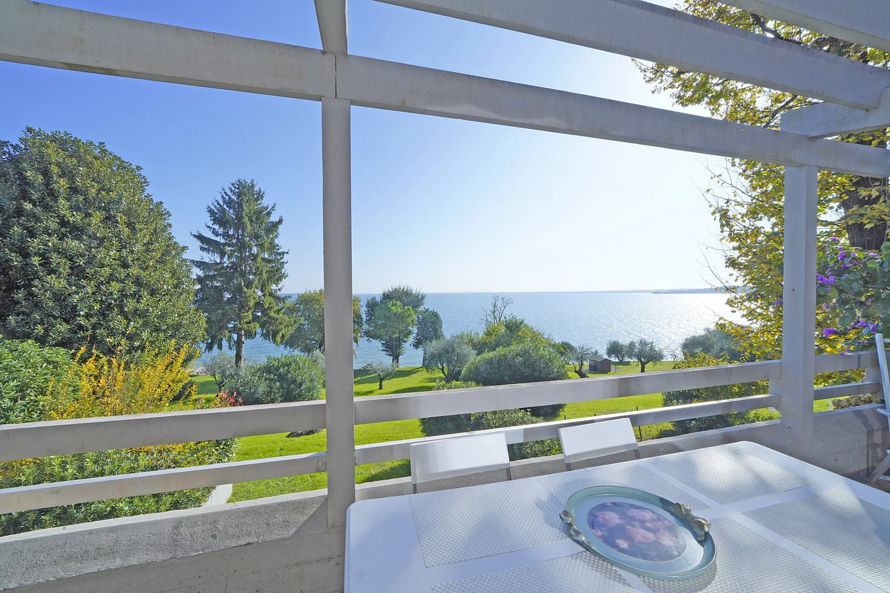 A sea-view terrace with a table, seating, and a garden beyond the railing.