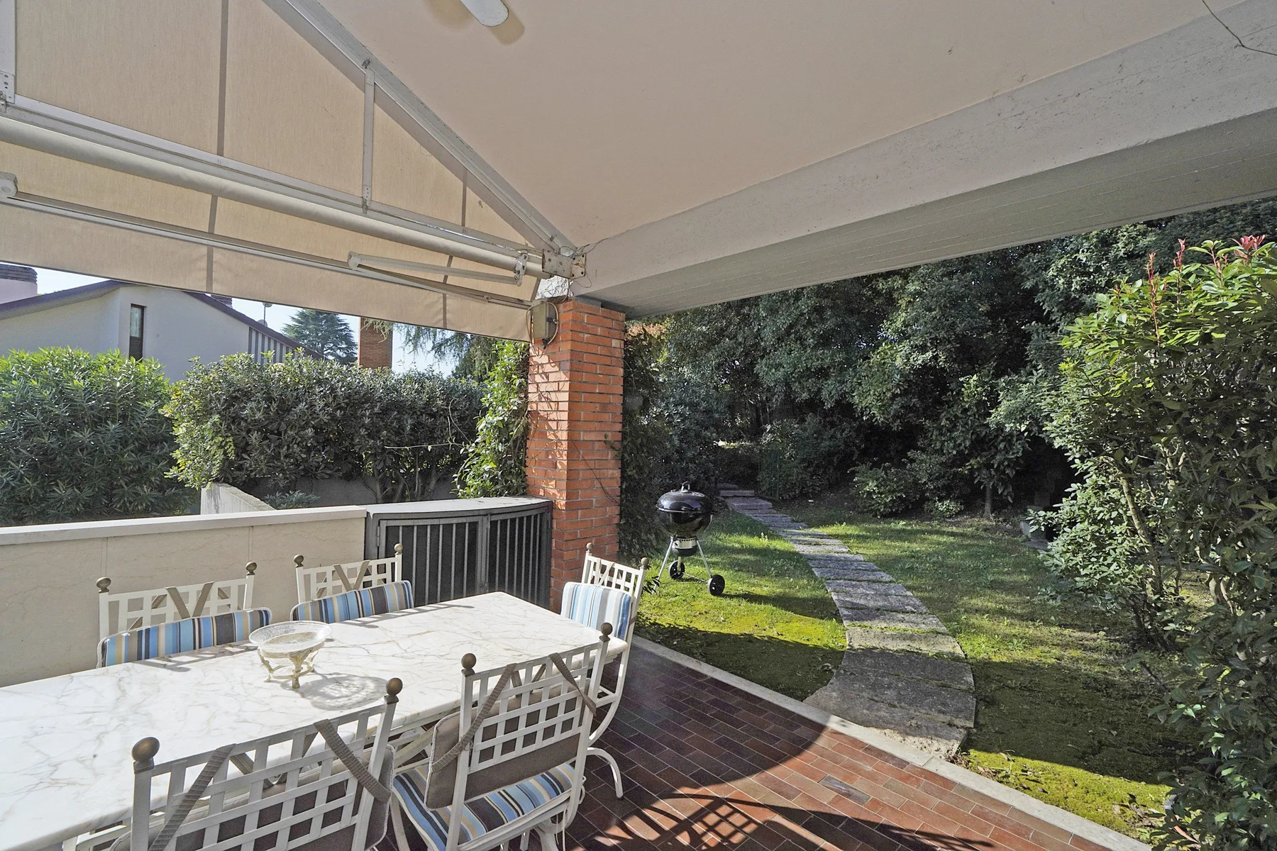 A covered patio with outdoor dining furniture opens onto a garden path.