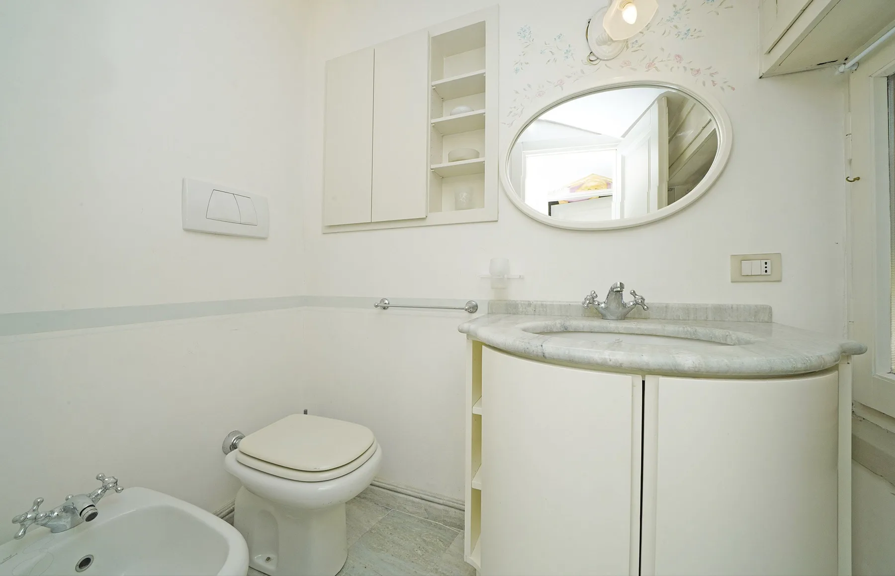 A bright bathroom with a sink, mirror, toilet, and bidet.