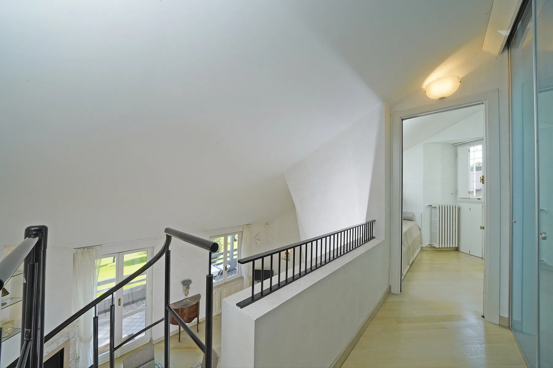 An upstairs hallway with a railing overlooks a bright lower-level area.