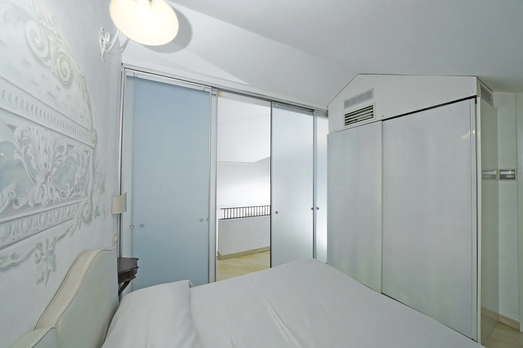 A bedroom with a bed beside sliding glass doors and a tall wardrobe.