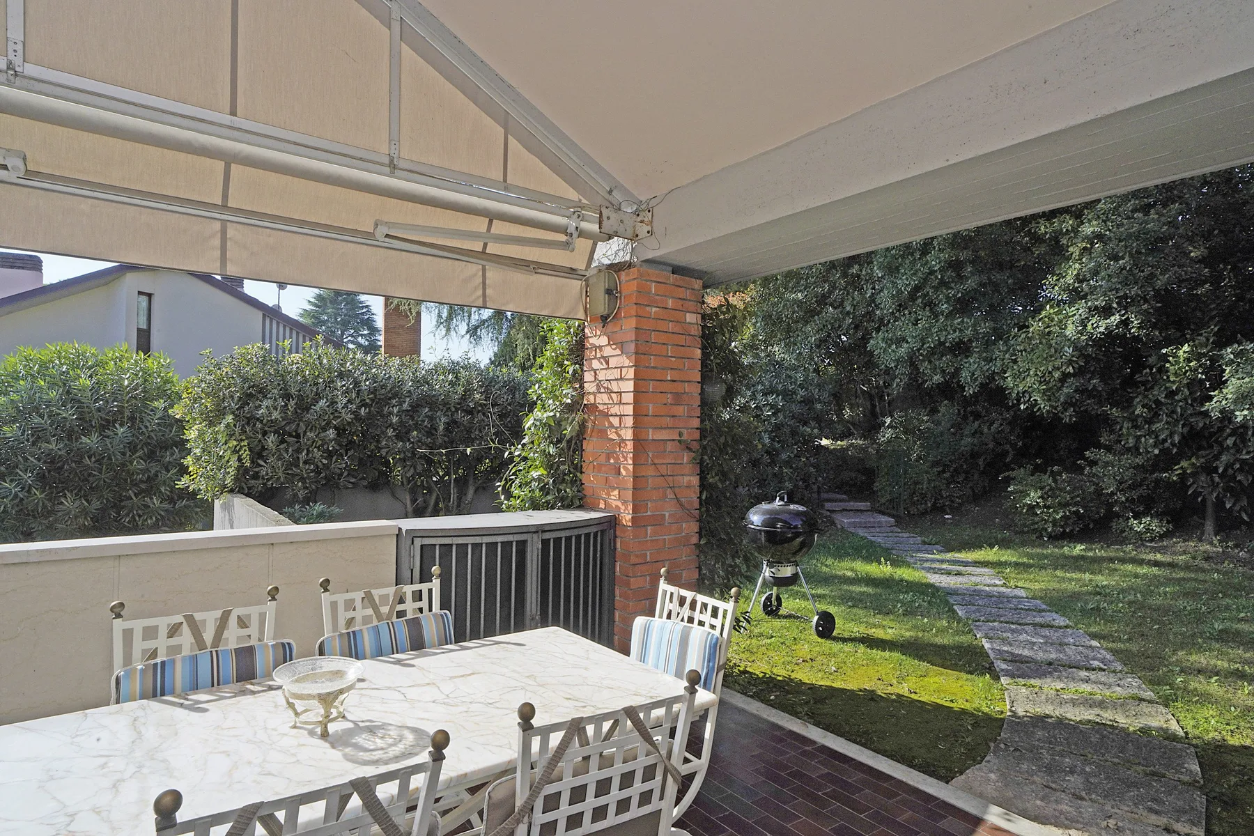 A covered patio with a dining table overlooks a grassy garden and stone path.