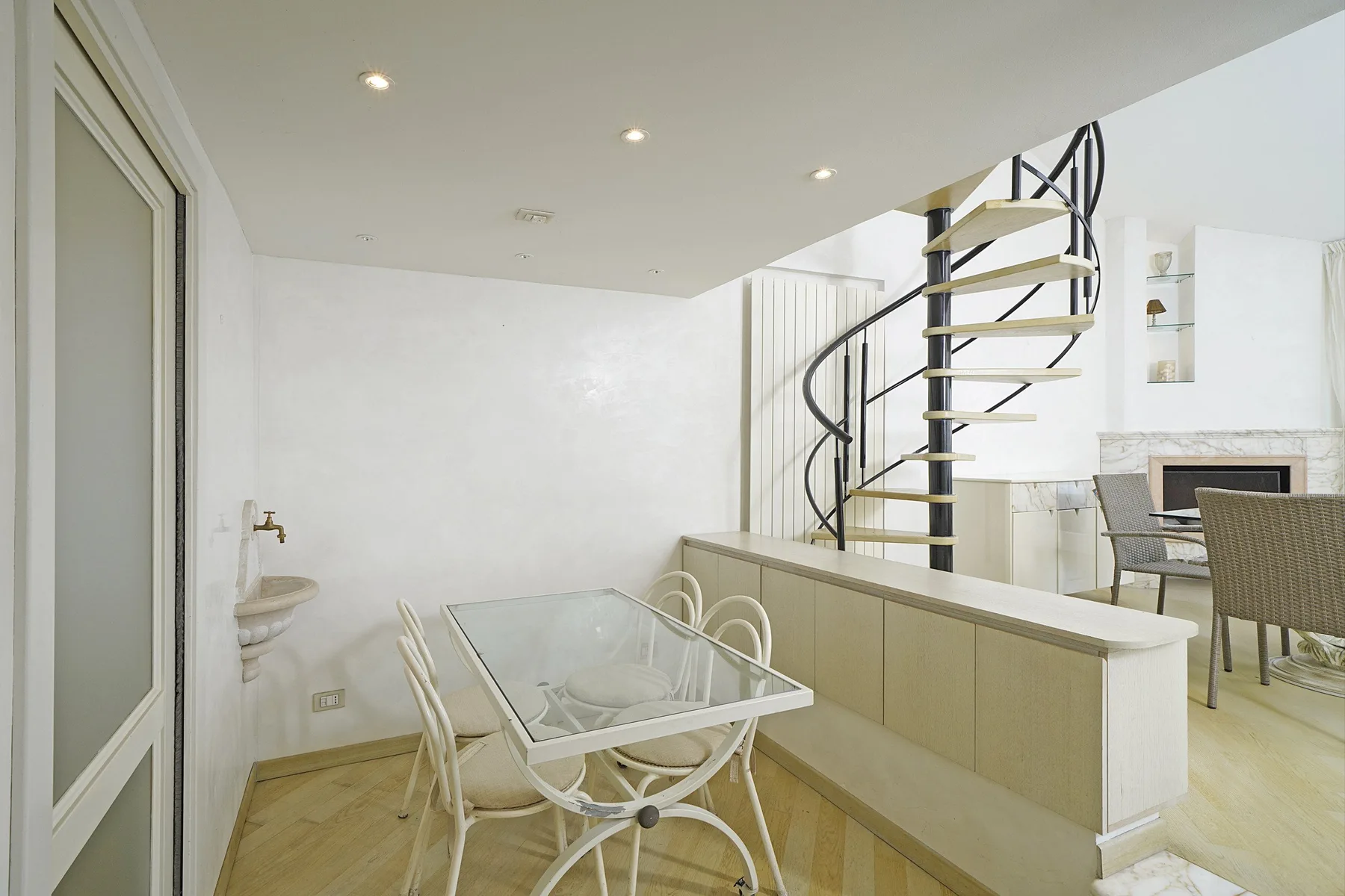 A dining area with a glass-top table beside a spiral staircase.