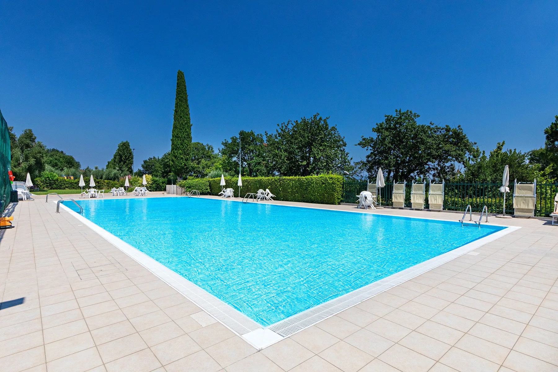 An outdoor swimming pool is surrounded by a broad paved deck and greenery.