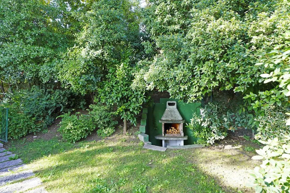 A leafy garden with a small outdoor fireplace beside the lawn.