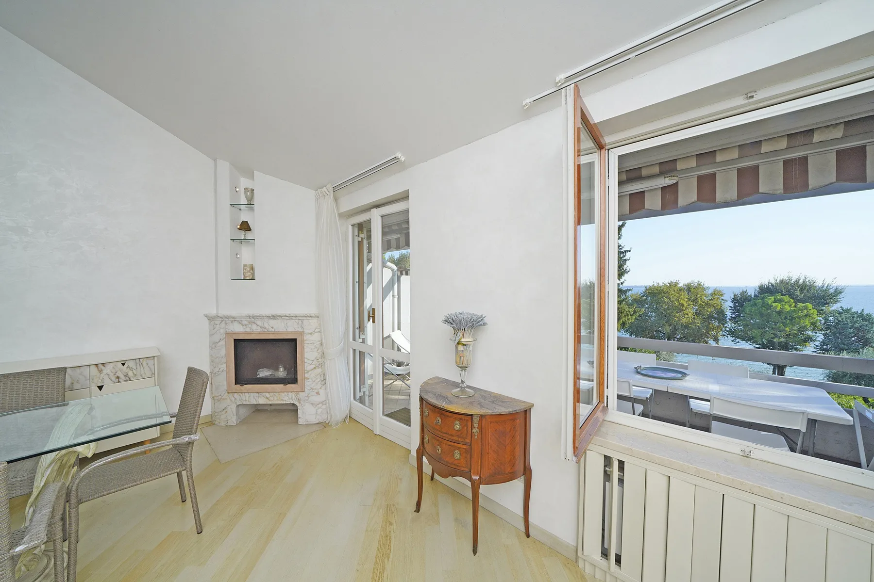 A bright sitting area opens onto a balcony with outdoor seating and greenery.