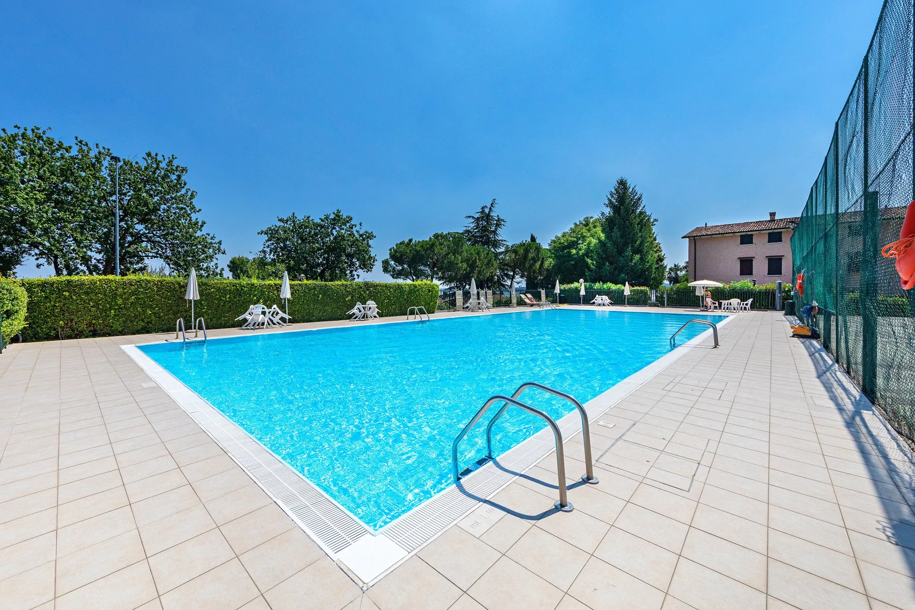 An outdoor swimming pool is surrounded by a tiled deck and greenery.