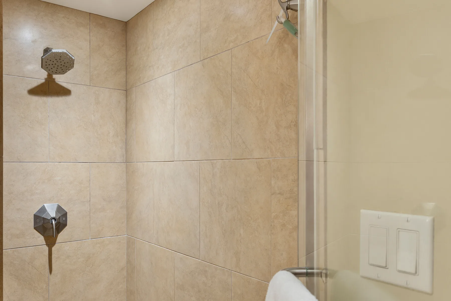 Una ducha con azulejos, cabezal y controles montados en la pared.