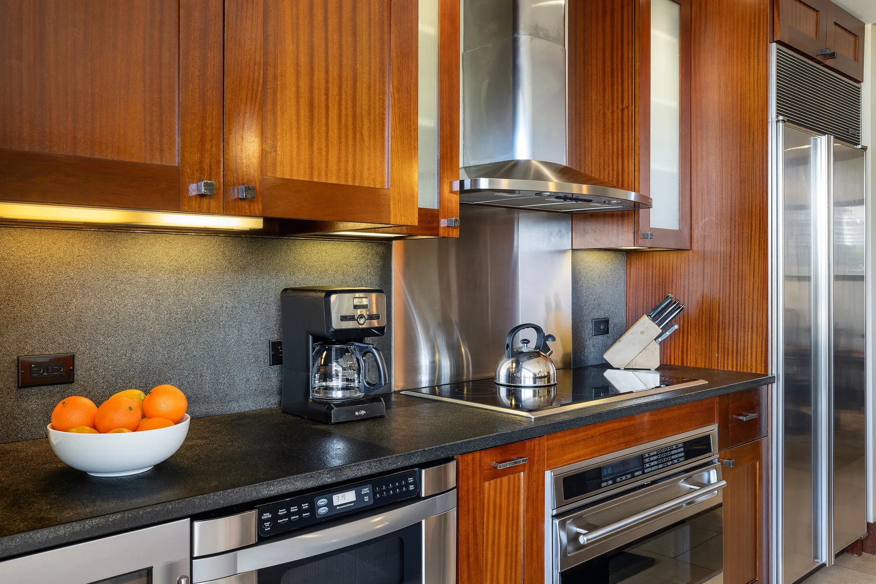 Una cocina con gabinetes de madera, encimeras oscuras y electrodomésticos de acero inoxidable.