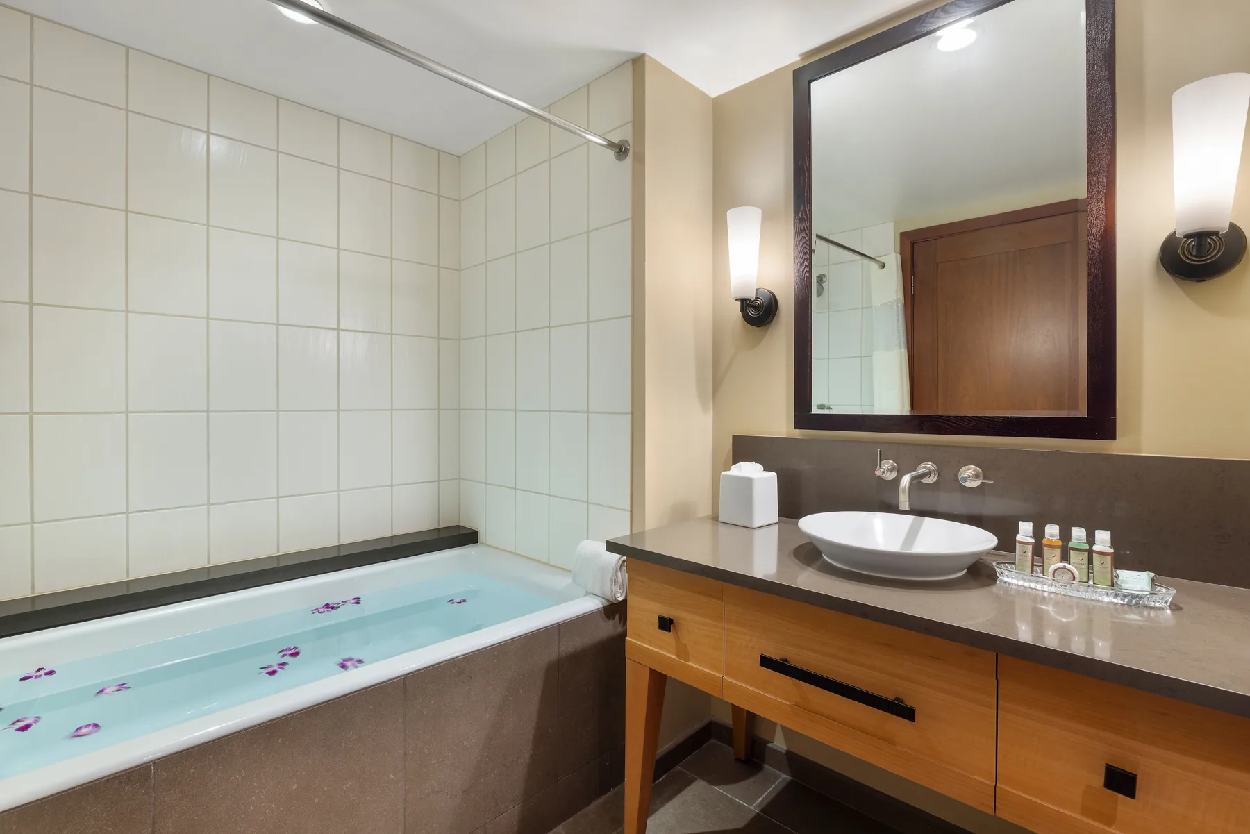 Baño con bañera y tocador bajo un espejo grande.