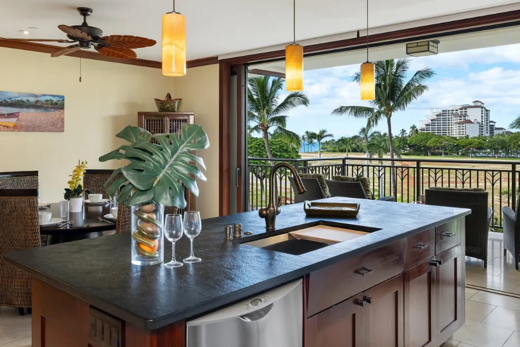 Una isla de cocina con una encimera oscura da a un balcón y palmeras.