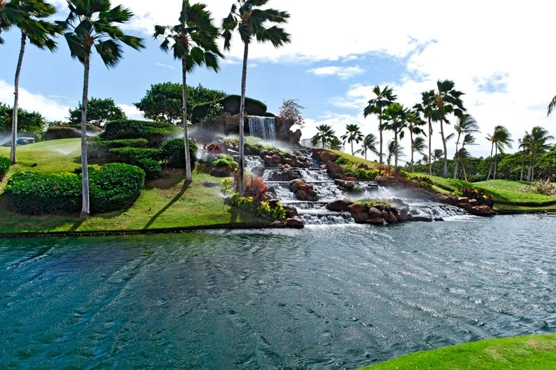 Una piscina ajardinada cuenta con una cascada y palmeras.