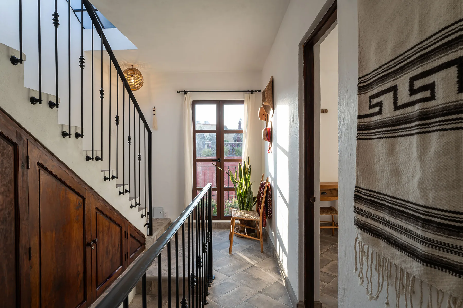 A bright interior hallway with a staircase, a window, and a woven wall hanging.
