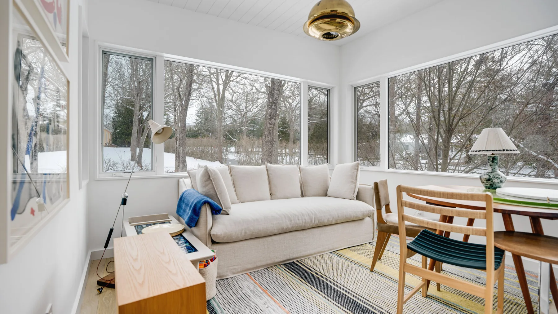 A bright living room with a sofa beside large windows overlooking trees.