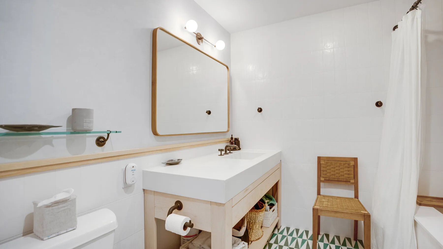 A bright bathroom with a white vanity, wall mirror, and patterned floor tiles.
