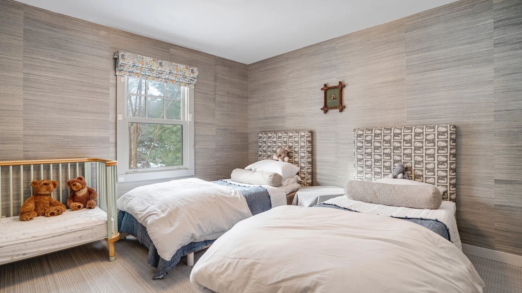 A bedroom with two beds and a window overlooking leafy trees.