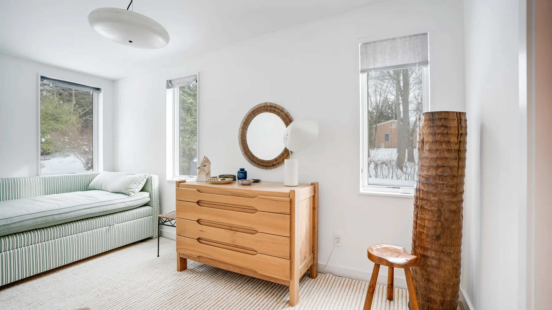 A bright bedroom with a bed, a wooden dresser, and a round mirror.