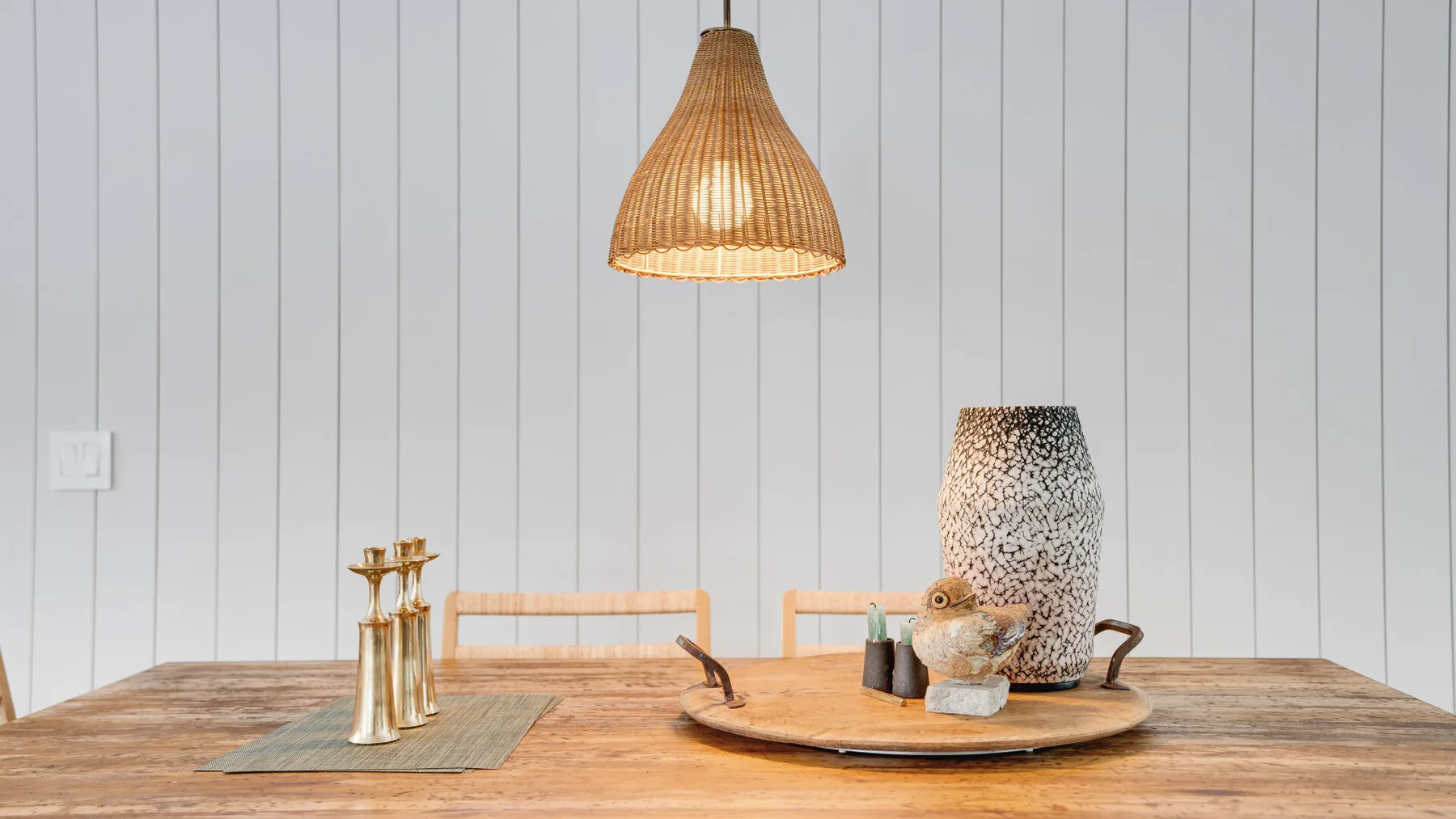 A dining table with a woven pendant lamp and decorative objects.