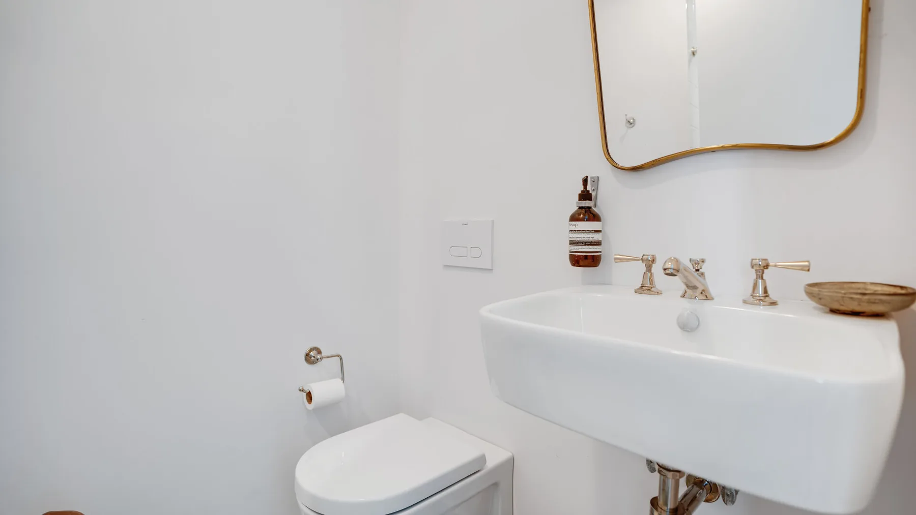 A bathroom with a wall-mounted sink, mirror, and toilet.